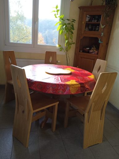 Une table ronde rouge avec des chaises en bois, près d'une fenêtre et d'une plante.